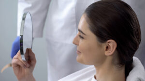 Woman looks happily at her reflection in the mirror following facial trauma and reconstructive surgery.